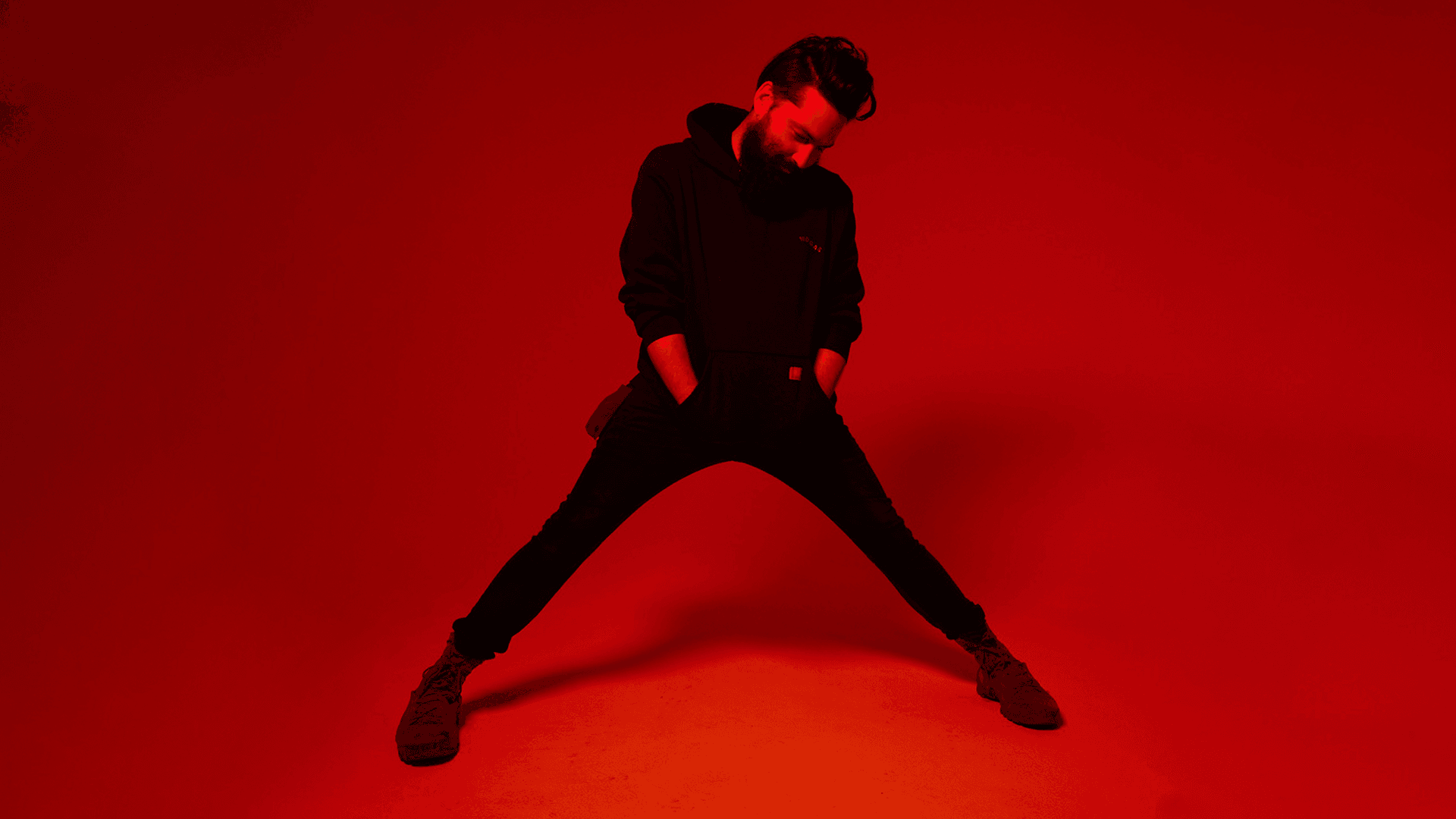 Boulevard Senior Art Director Wood Simmons, lit all in red on a blank studio background, stands in a broad stance with hands stuffed into his hoody pocket.