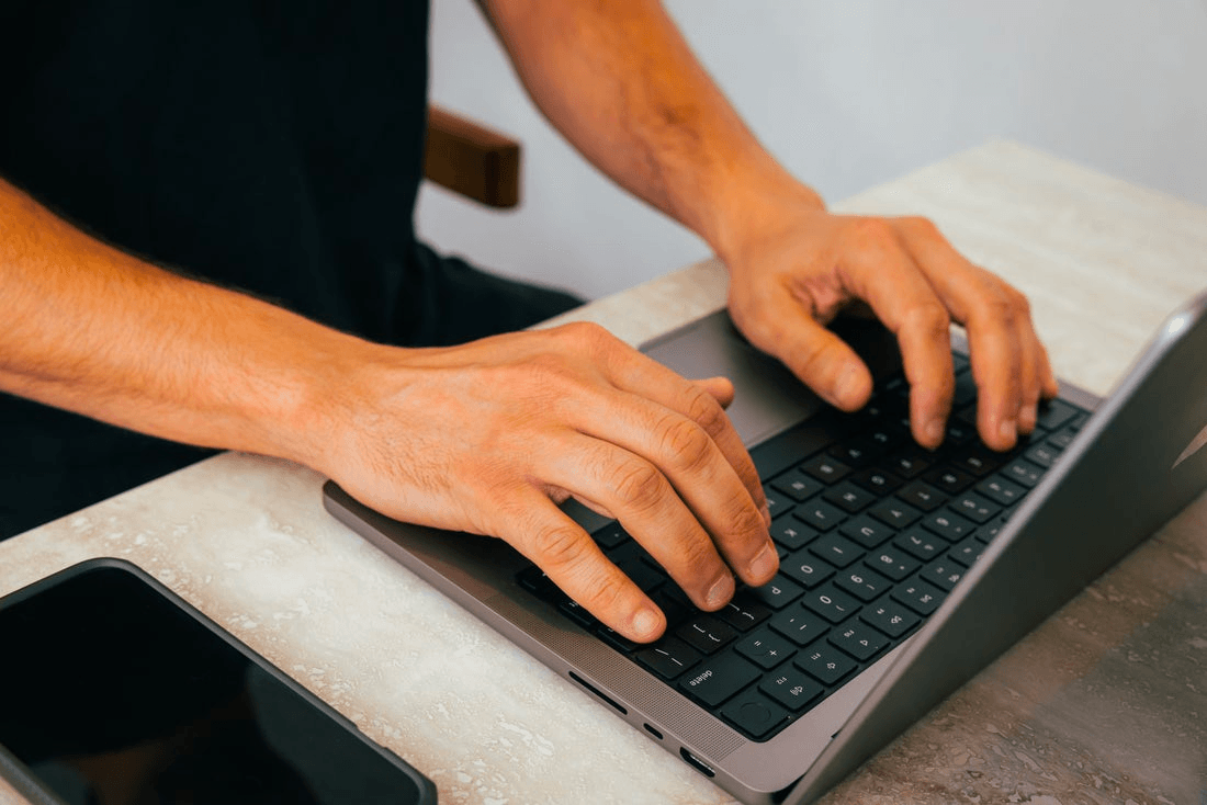 A person's hands type on a MacBook keyboard.