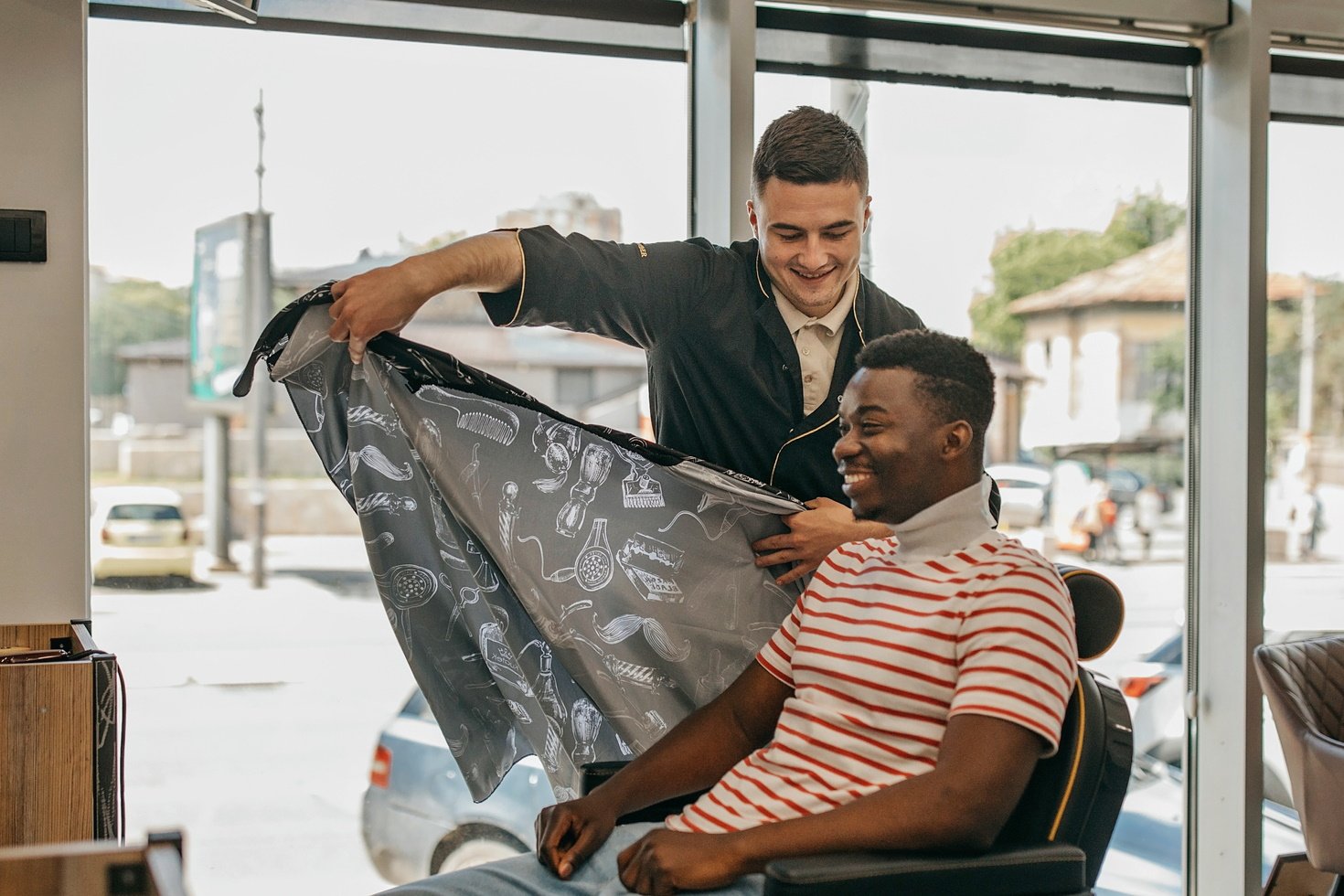 A man smiles as a barber prepares him for a haircut appointment.