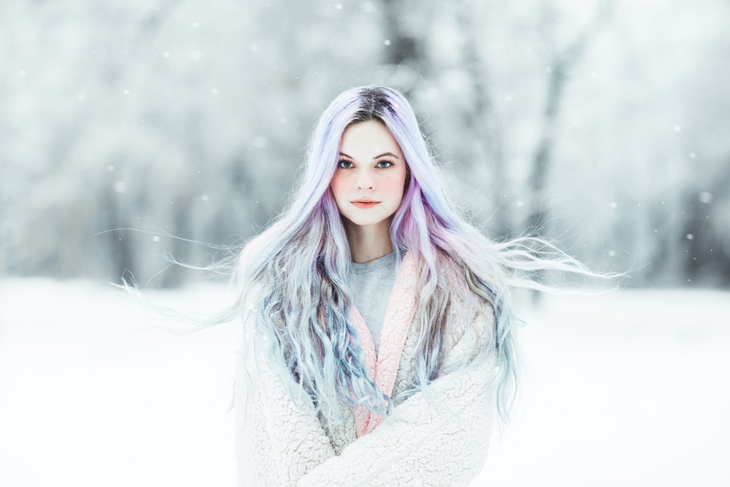 A woman with platinum and pastel hair stands in a snowy field looking straight out of a fantasy novel.