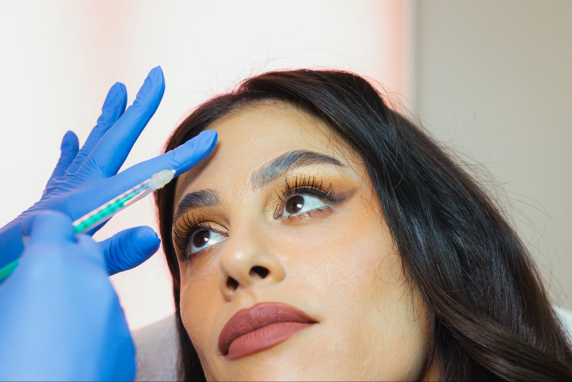 A medical aesthetician performs injections on a woman's forehead.