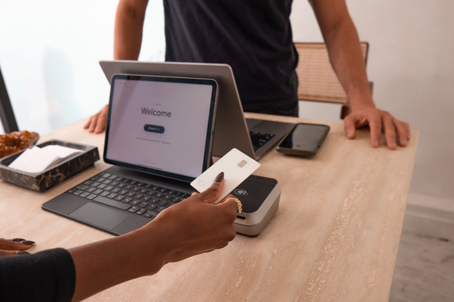 A well-manicured hand holds a credit card as a salon employee prepares to process a payment.