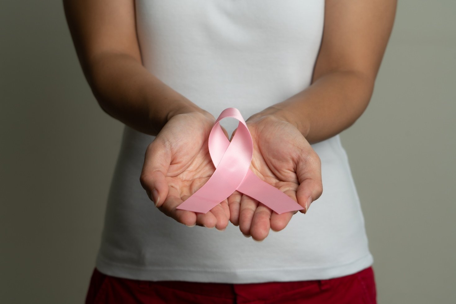 Woman with outstretched hands holding a large pink breast cancer ribbon.