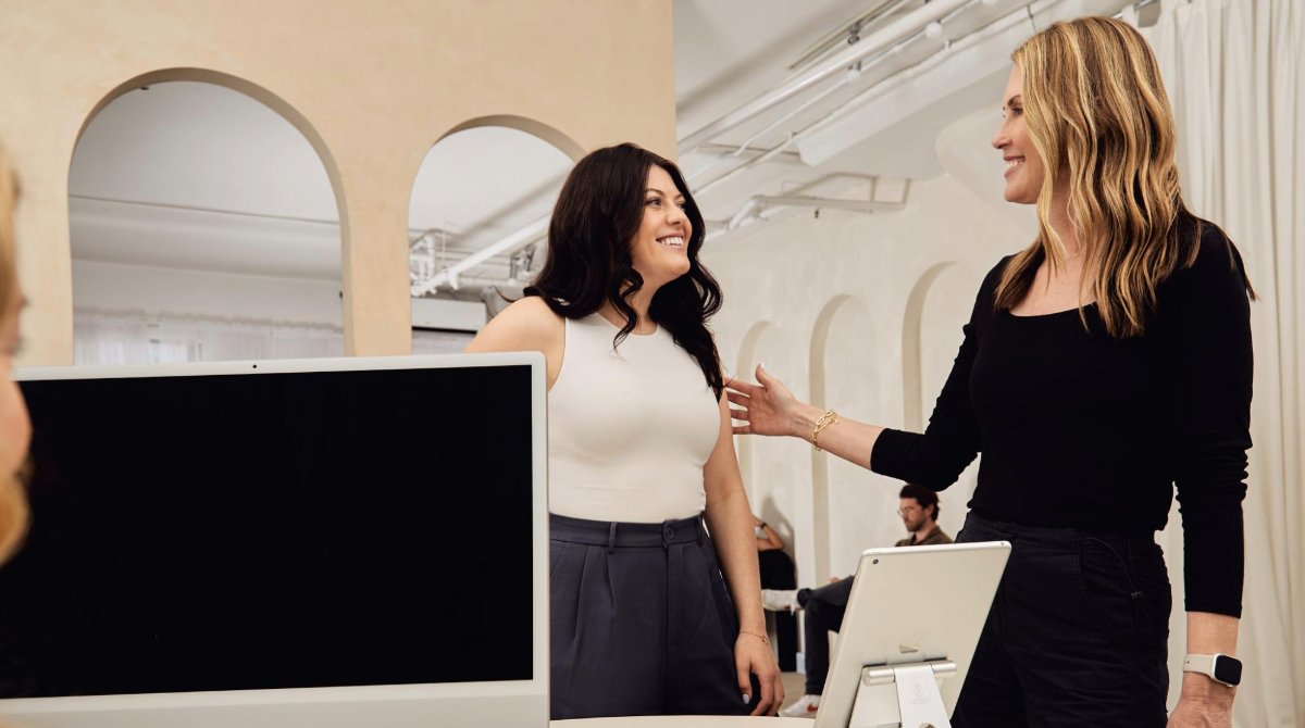 A salon owner and her client stand in front of the reception desk. A receptionist sits in front of a computer next to the Boulevard Duo payment processor and a tablet.