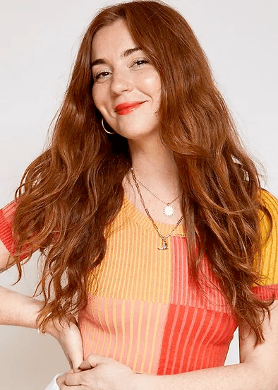 A publicity photo of Jenna Perry from the waist up. She's smiling as her effortlessly wavy hair falls over her shoulders.