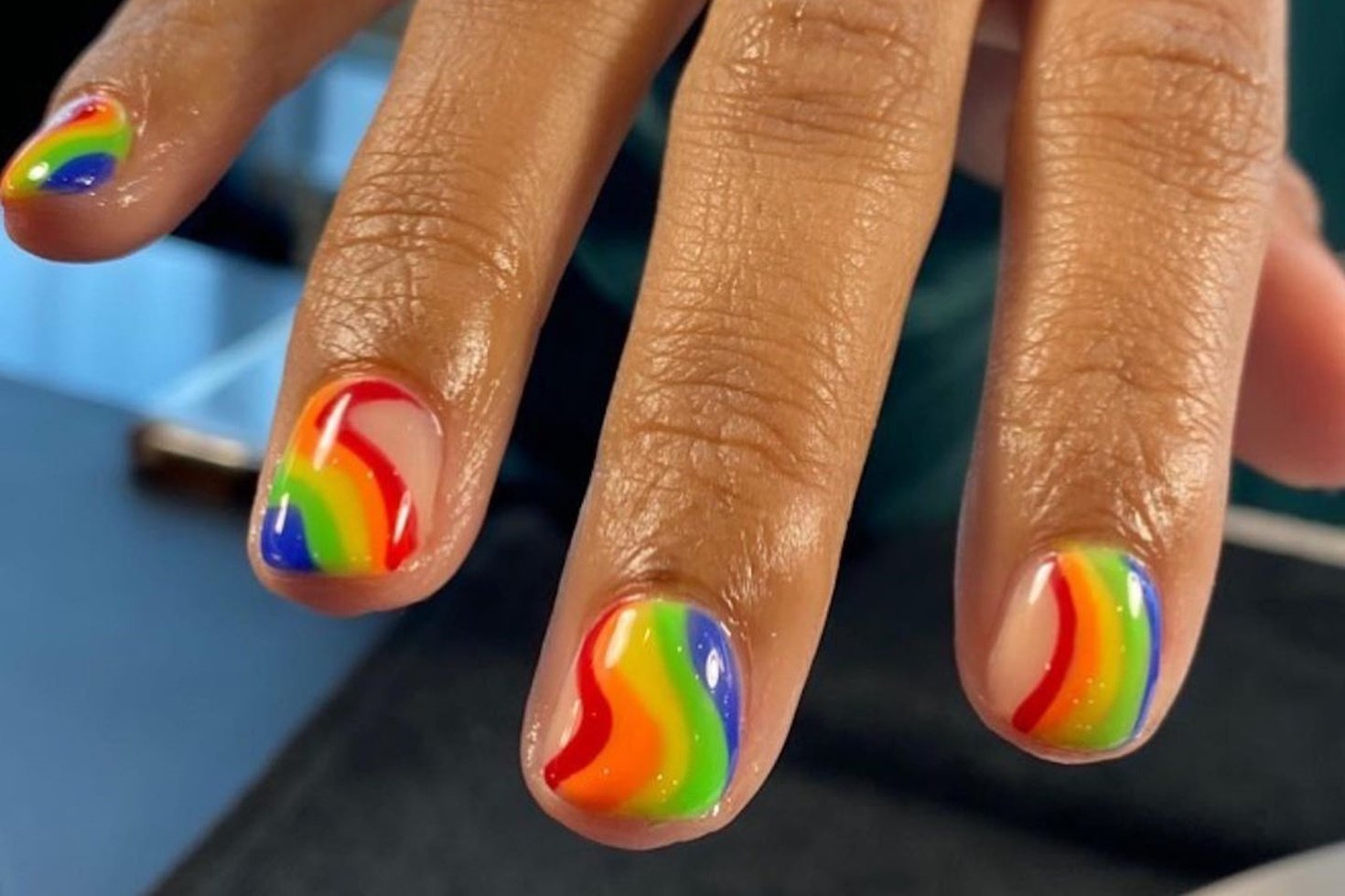 A well-manicured right hand extends for a picture with nails painted in rainbow colors.