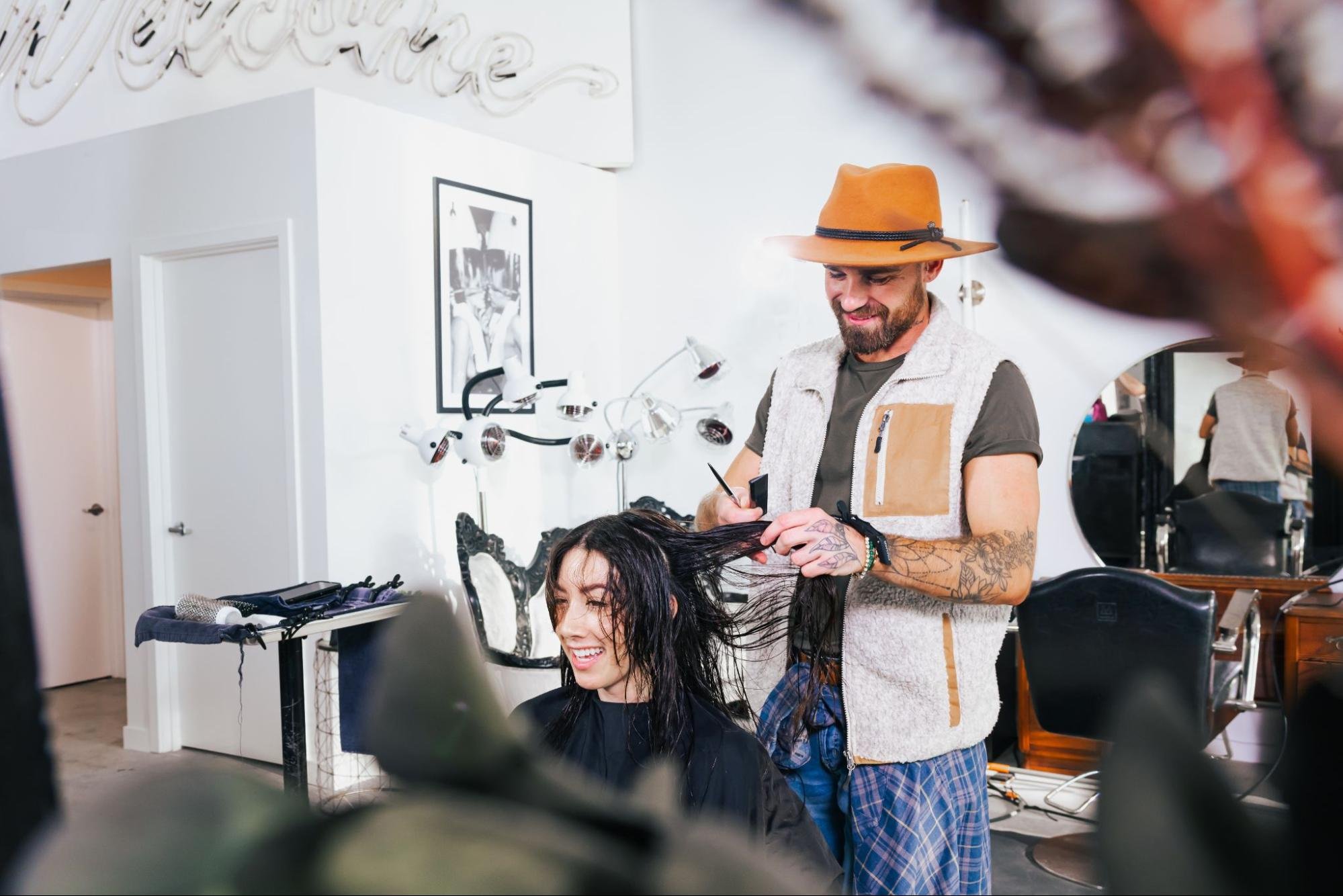 A man wearing an orange hat cuts the hair of a young woman
