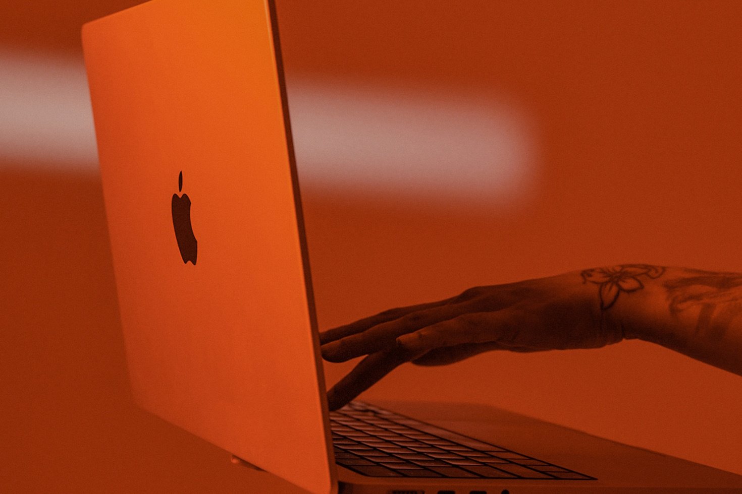 One hand supports an Apple laptop while another hand types on the keyboard.