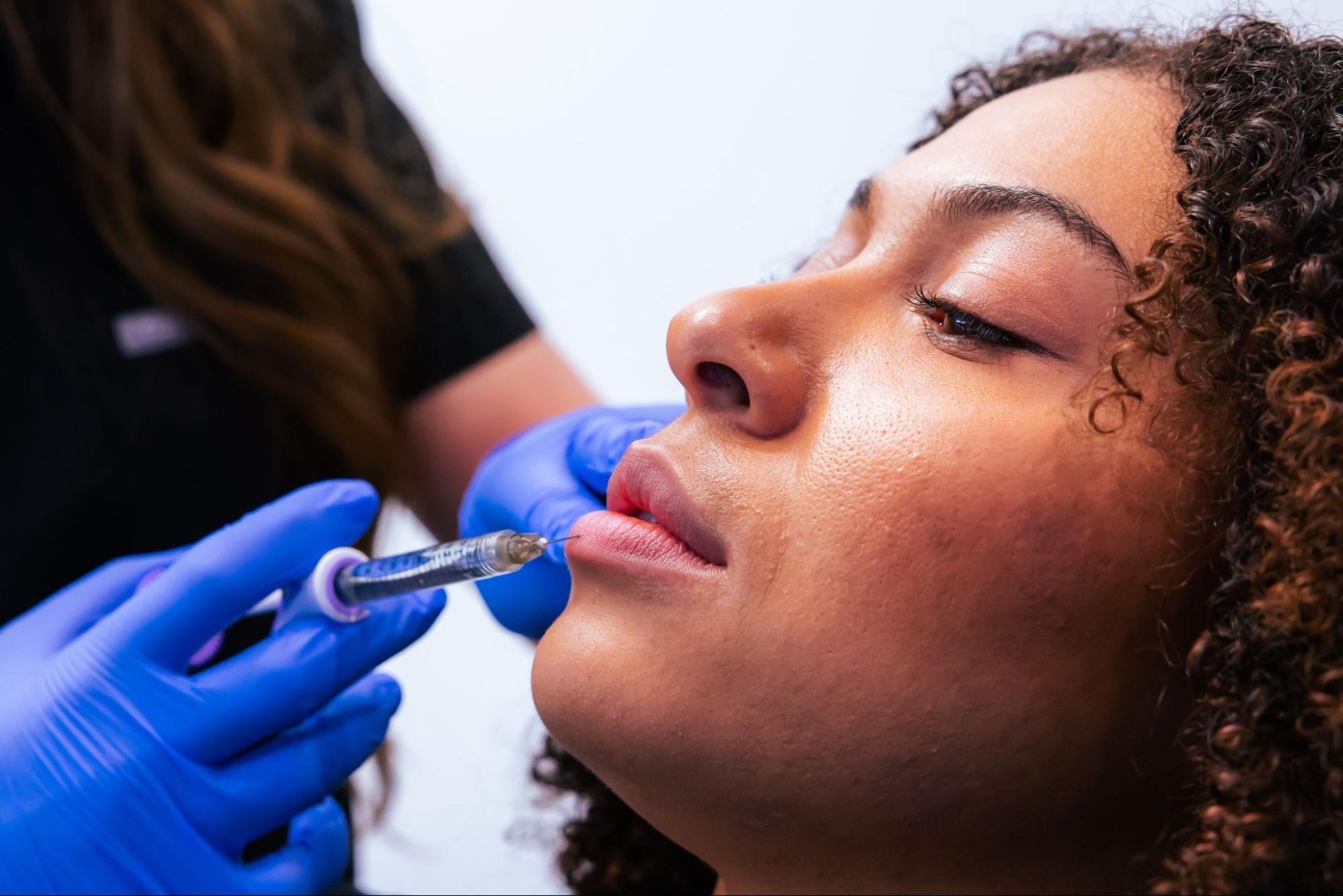 A medspa employee gives a patient an injection into their lower lip.