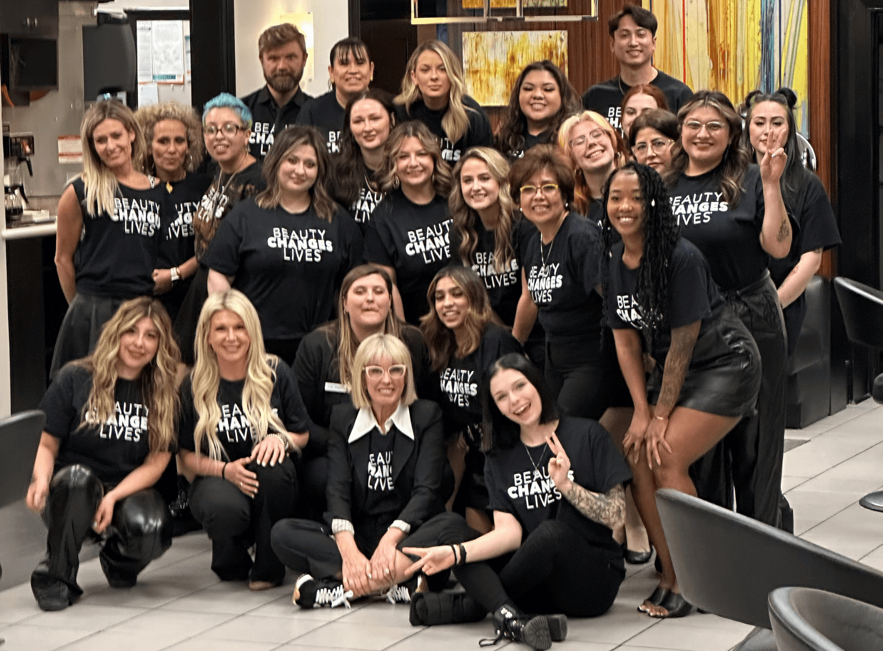A group of mentors and mentees pose for a picture wearing "Beauty Changes Lives" t-shirts.