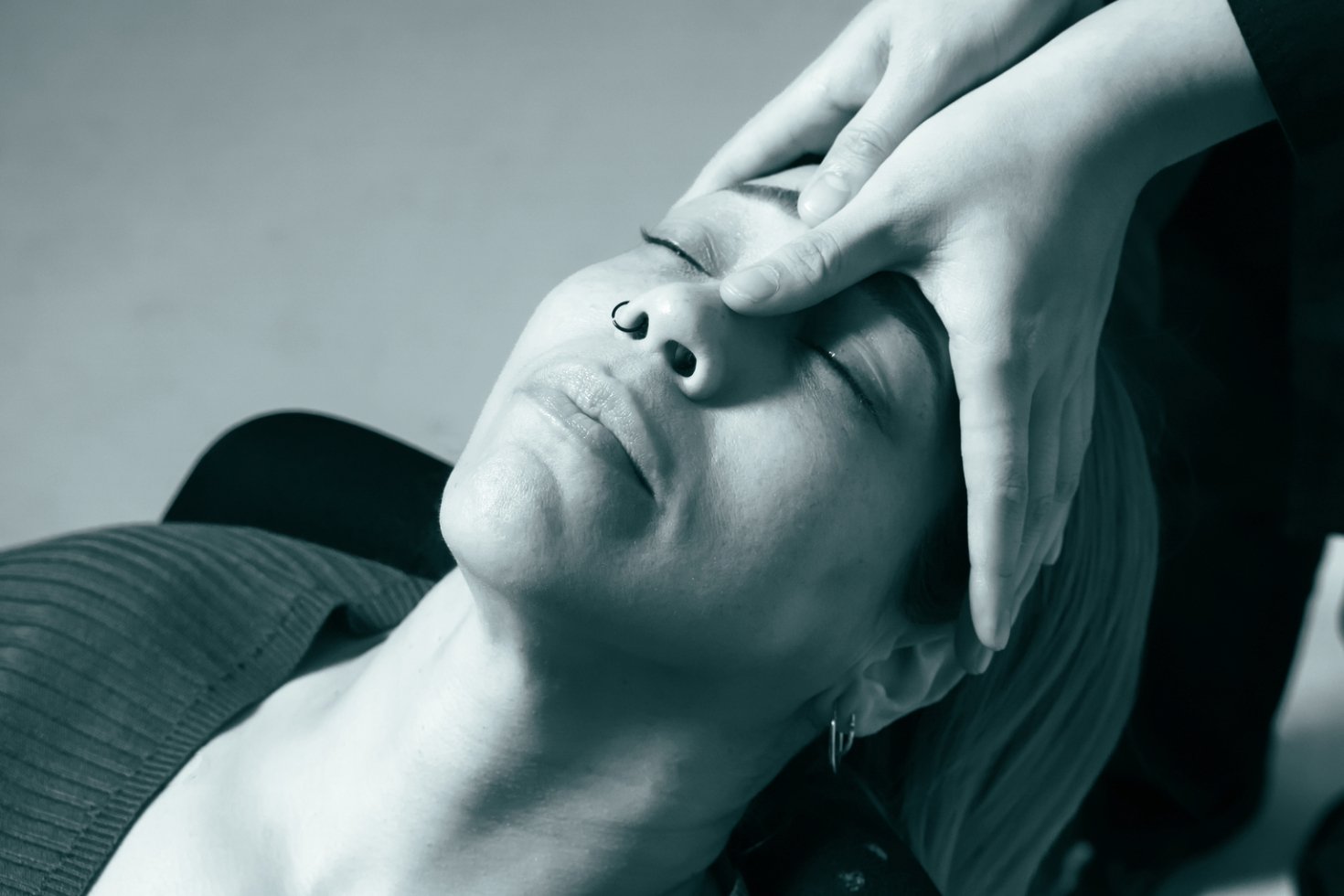 A black-and-white photo of a woman leaning back in a chair with her eyes closed. A specialist's hands are on her face.