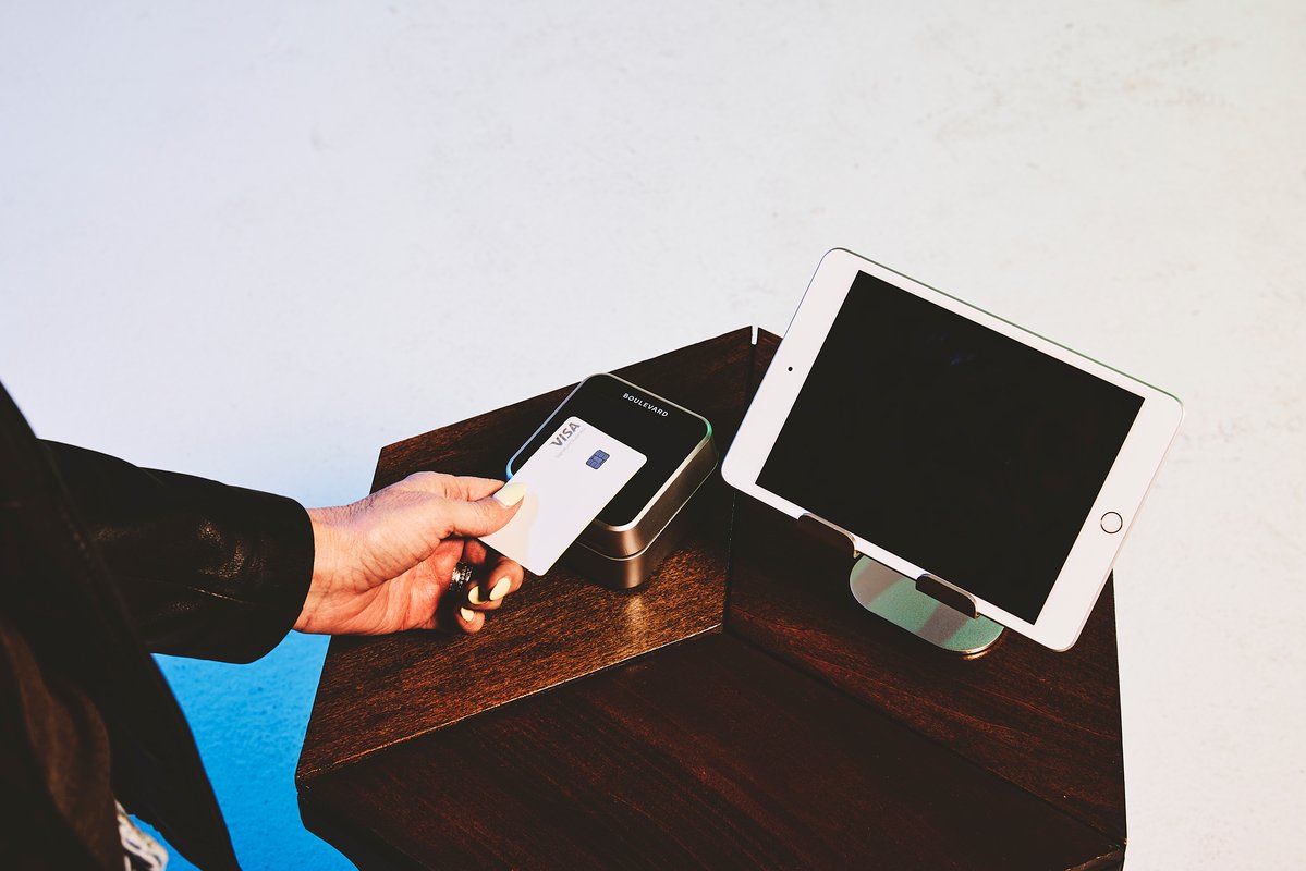A woman holding a credit card to a payment terminal to pay for her self-care service.